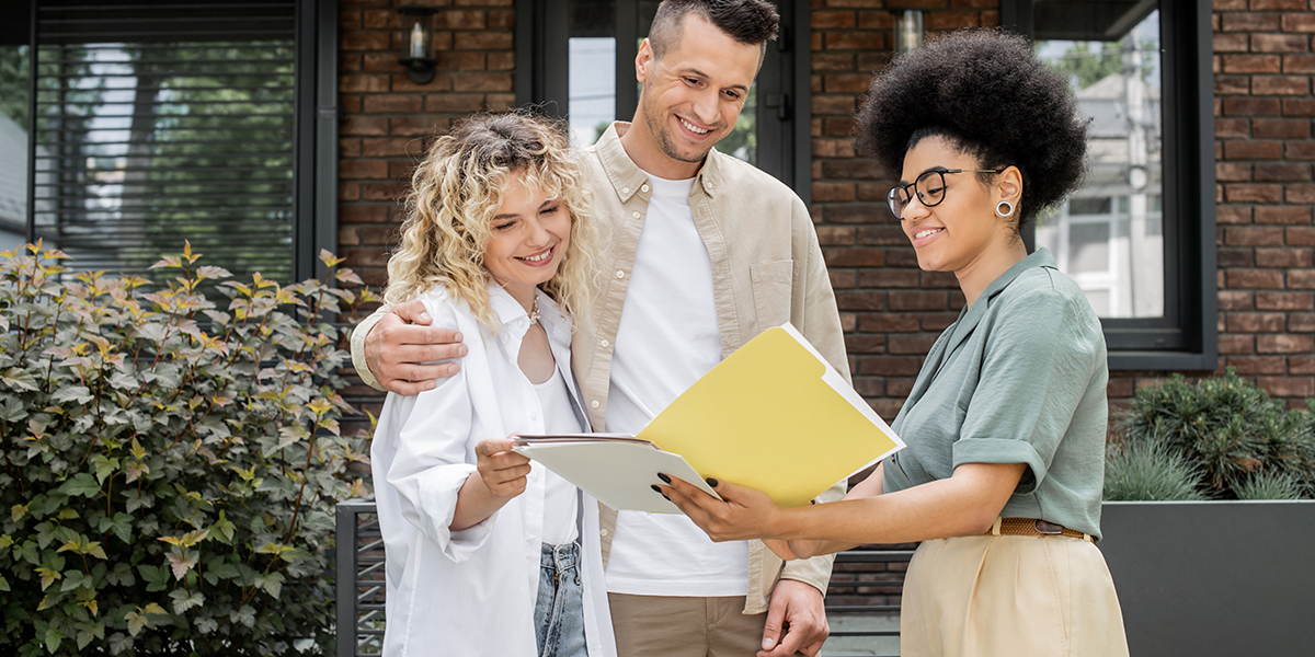 african american property realtor showing documents to happy couple